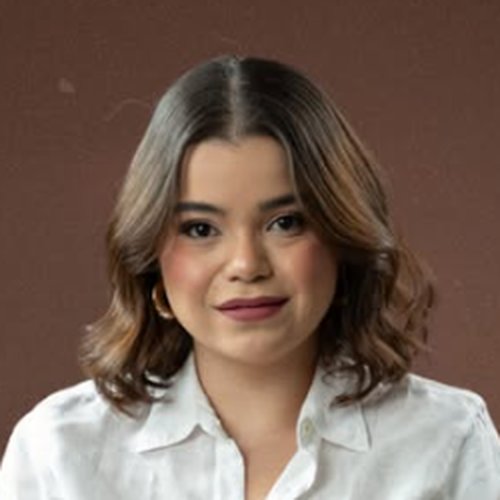 Dra. Maria Vitória sorrindo levemente, de camisa branca, em fundo marrom