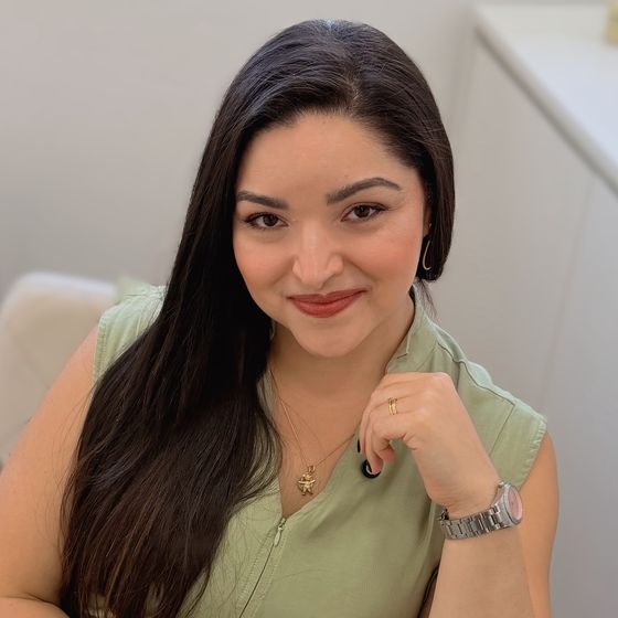 Dra. Mayara Viana sorrindo, sentada numa poltrona, com macacão verde-sálvia
